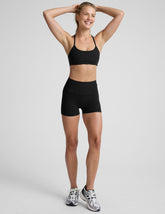 woman wearing a black sports bra and black 3" biker shorts on a plain background.